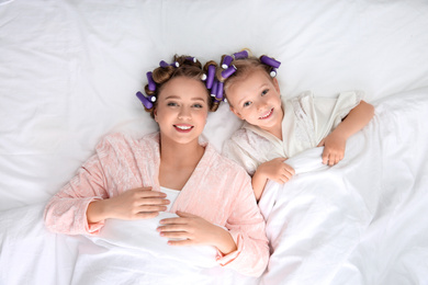 Happy mother and daughter with curlers lying on bed, top view