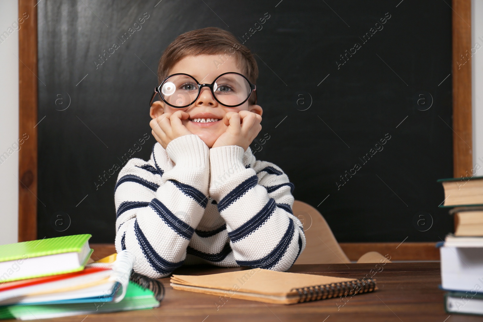 Photo of Cute little child wearing glasses at desk in classroom. First time at school