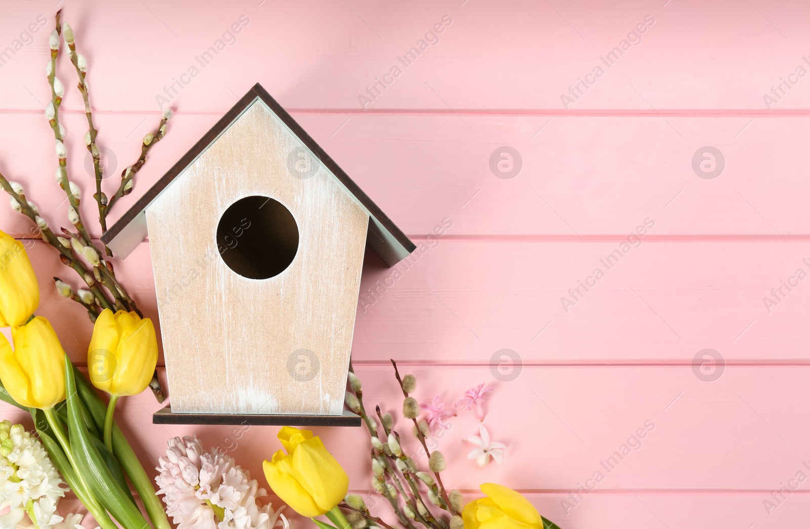 Photo of Flat lay composition with bird house and flowers on pink wooden background. Space for text