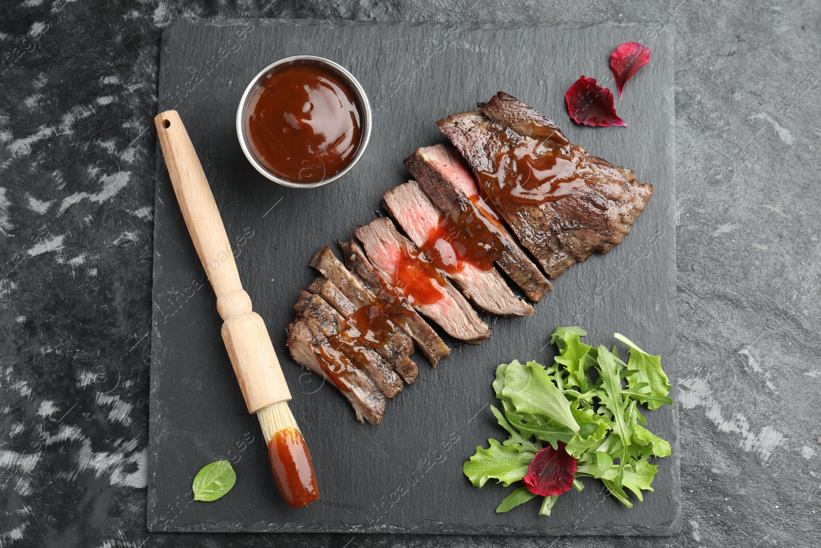 Photo of Pieces of delicious roasted beef meat with sauce and greens on black table, top view