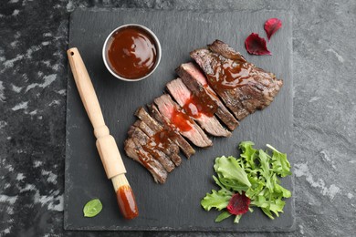 Pieces of delicious roasted beef meat with sauce and greens on black table, top view