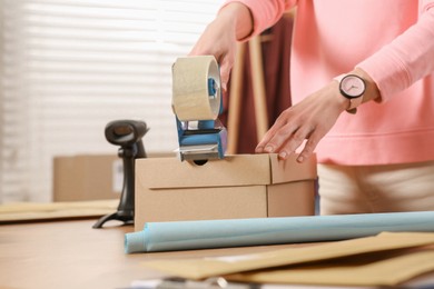 Photo of Seller taping parcel at workplace, closeup. Online store