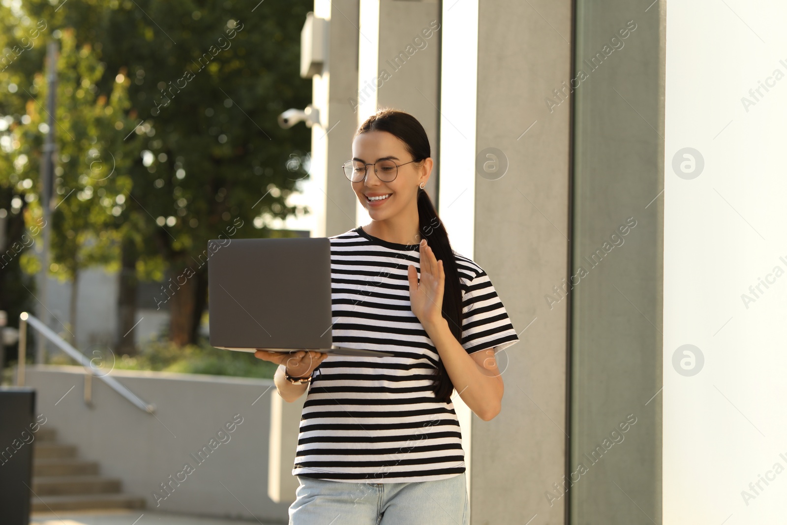 Photo of Happy young woman using modern laptop for video call outdoors