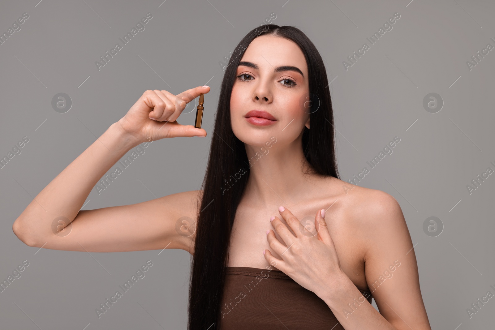 Photo of Beautiful young woman holding skincare ampoule on grey background