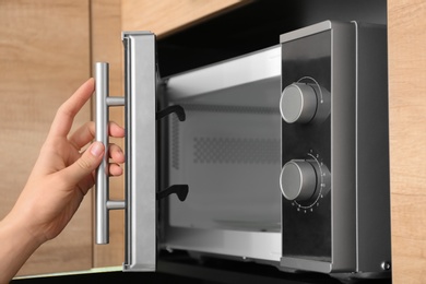 Young woman using microwave oven in kitchen, closeup