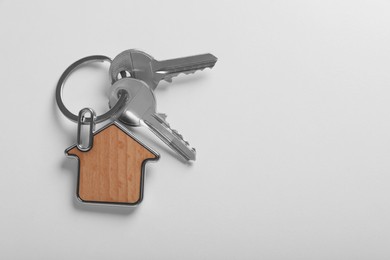 Photo of Keys with trinket in shape of house on white background, top view and space for text. Real estate agent services