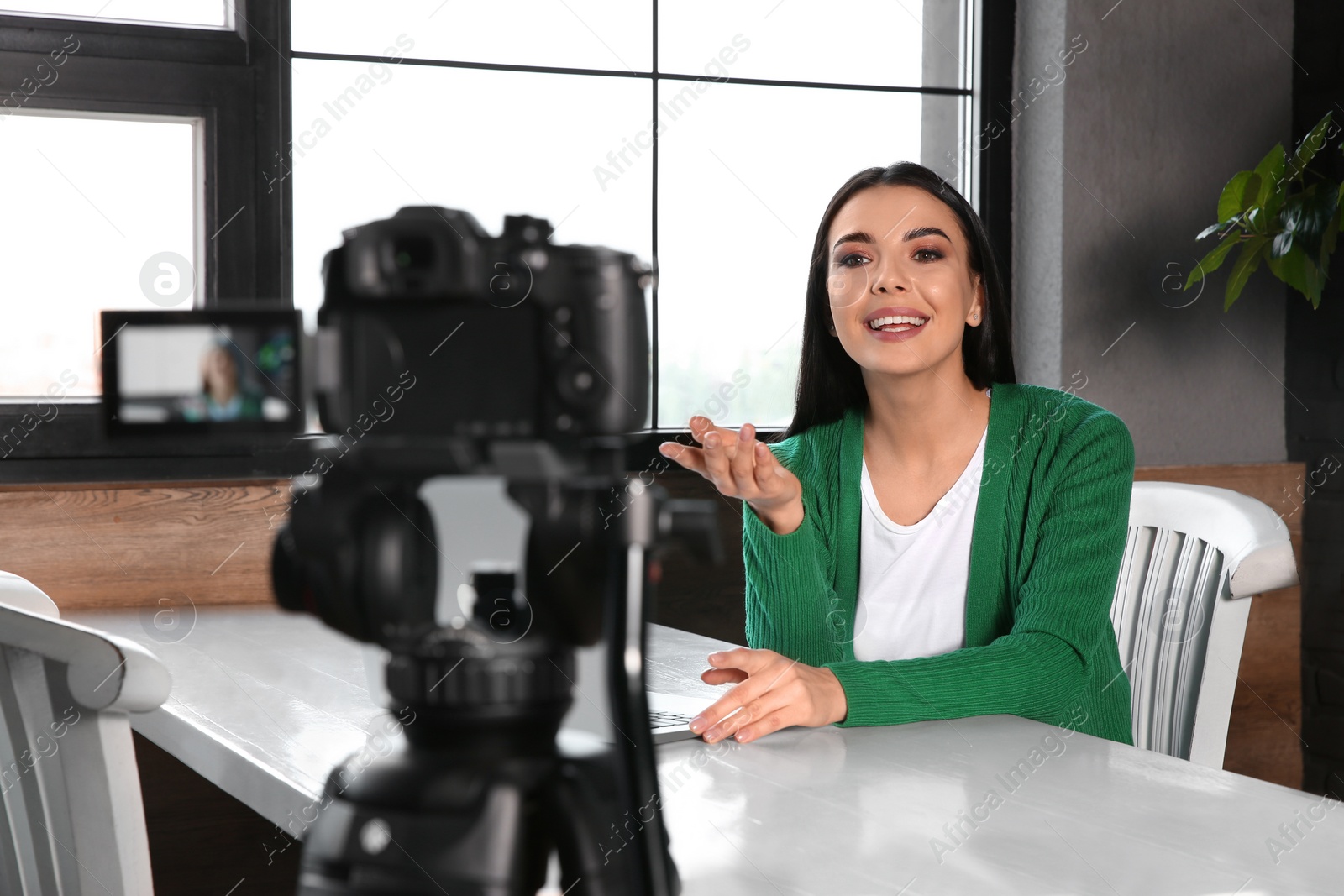 Photo of Young blogger with laptop recording video on camera at cafe