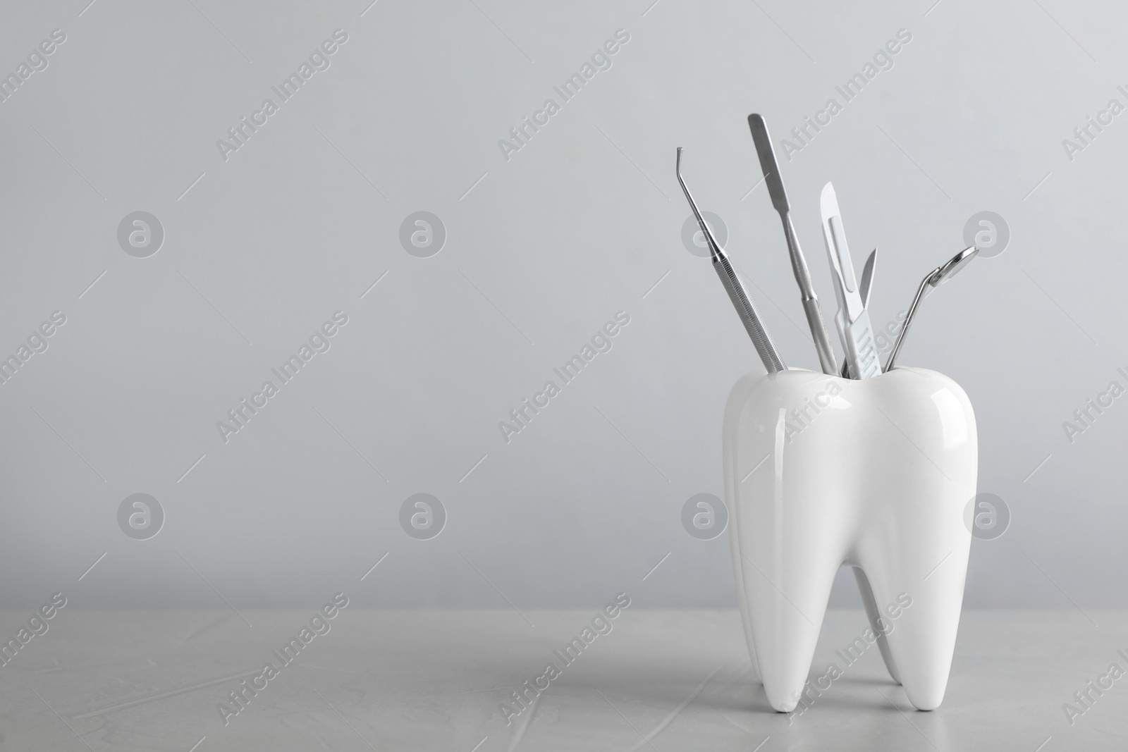 Photo of Tooth shaped holder with dentist's tools on light grey table. Space for text
