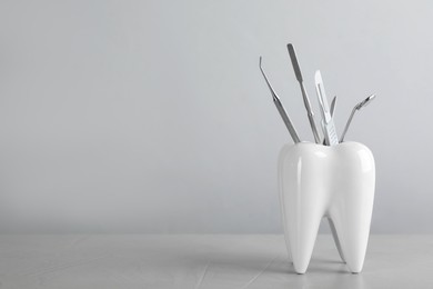 Photo of Tooth shaped holder with dentist's tools on light grey table. Space for text