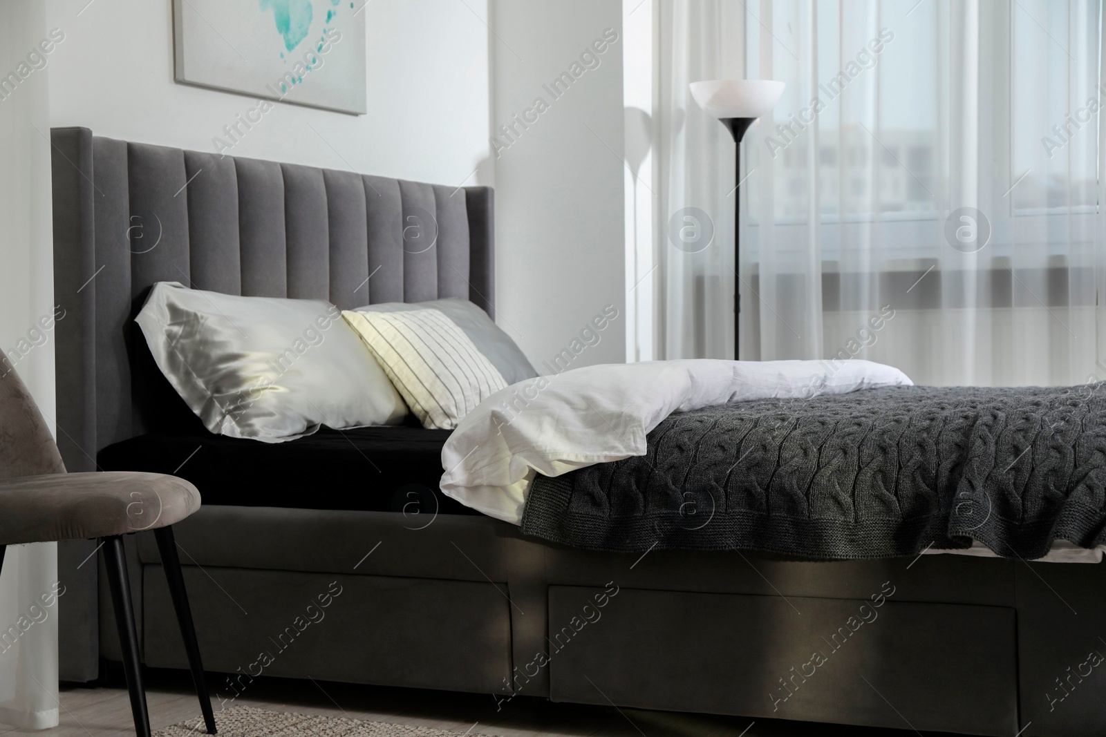 Photo of Stylish bedroom interior with large bed, lamp and chair