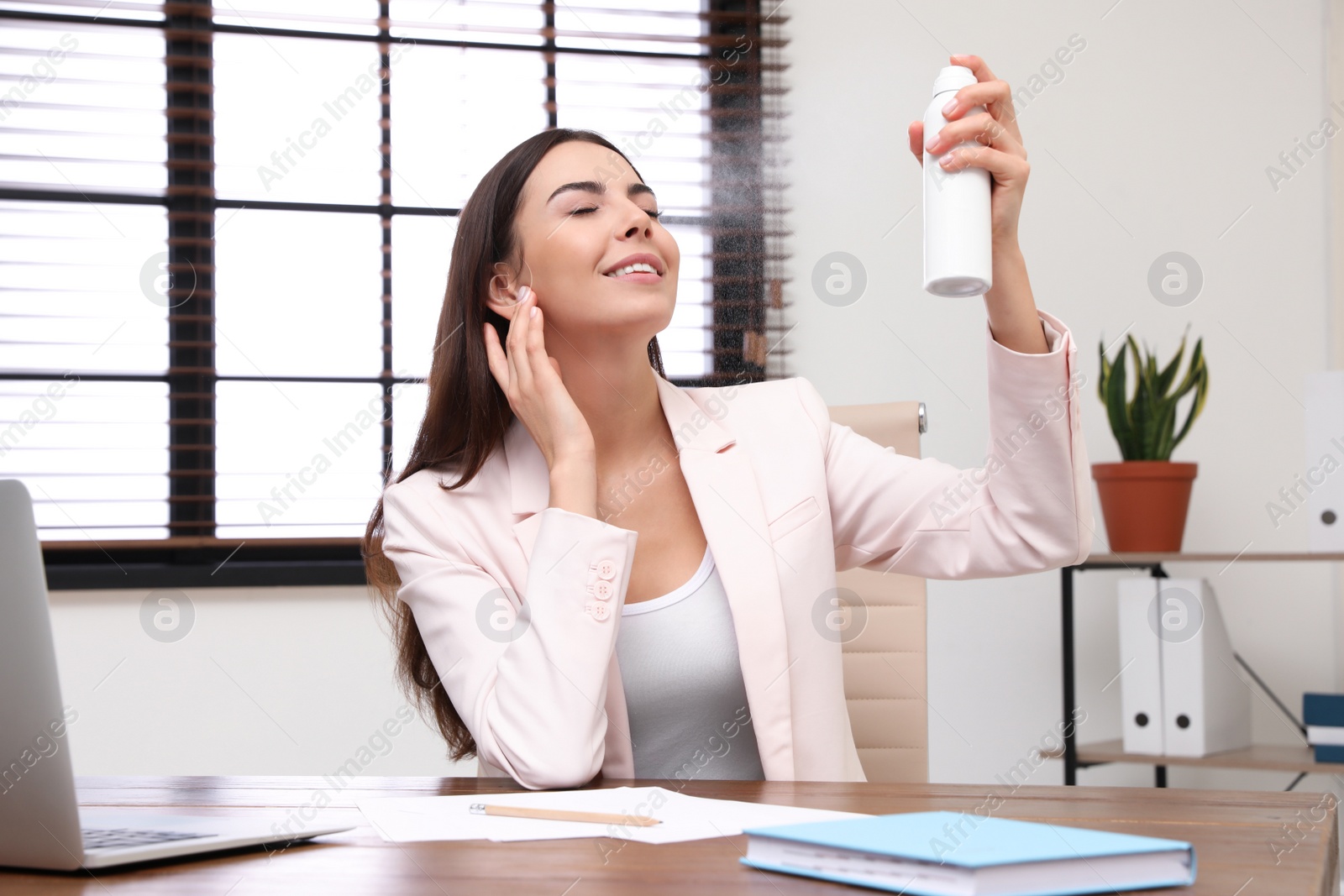 Photo of Young woman applying thermal water on face in office. Cosmetic product