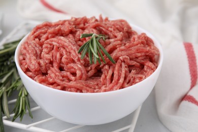 Photo of Fresh raw ground meat and rosemary in bowl on table, closeup