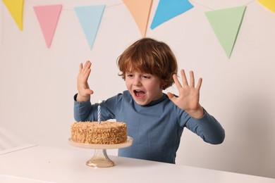 Cute boy with birthday cake at white table indoors