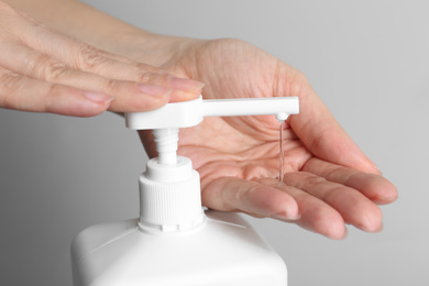 Photo of Woman applying antiseptic gel on hand against grey background, closeup
