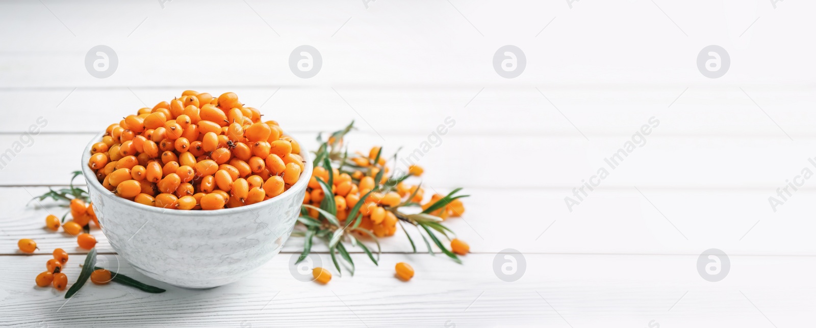 Image of Fresh ripe sea buckthorn in bowl on white wooden table, space for text. Banner design