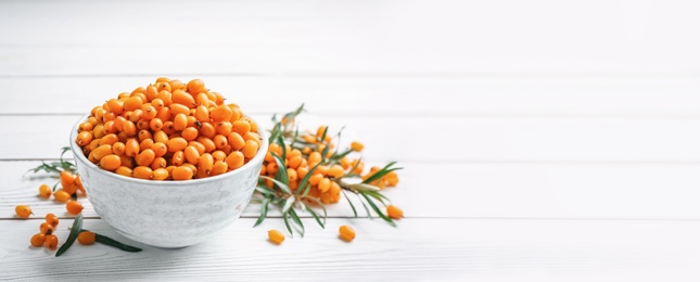 Image of Fresh ripe sea buckthorn in bowl on white wooden table, space for text. Banner design