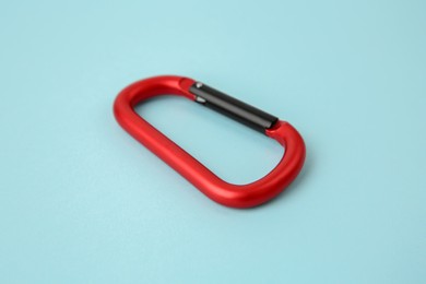 Photo of One red carabiner on light blue background, closeup