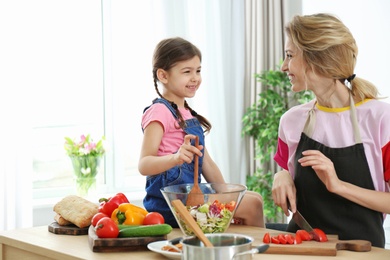 Young nanny with cute little girl cooking together in kitchen