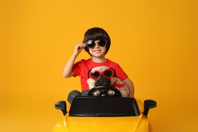 Photo of Little boy with his dog in toy car on yellow background