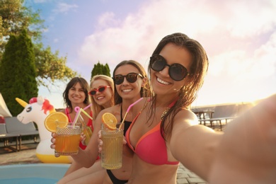 Happy women with refreshing drinks taking selfie at pool party
