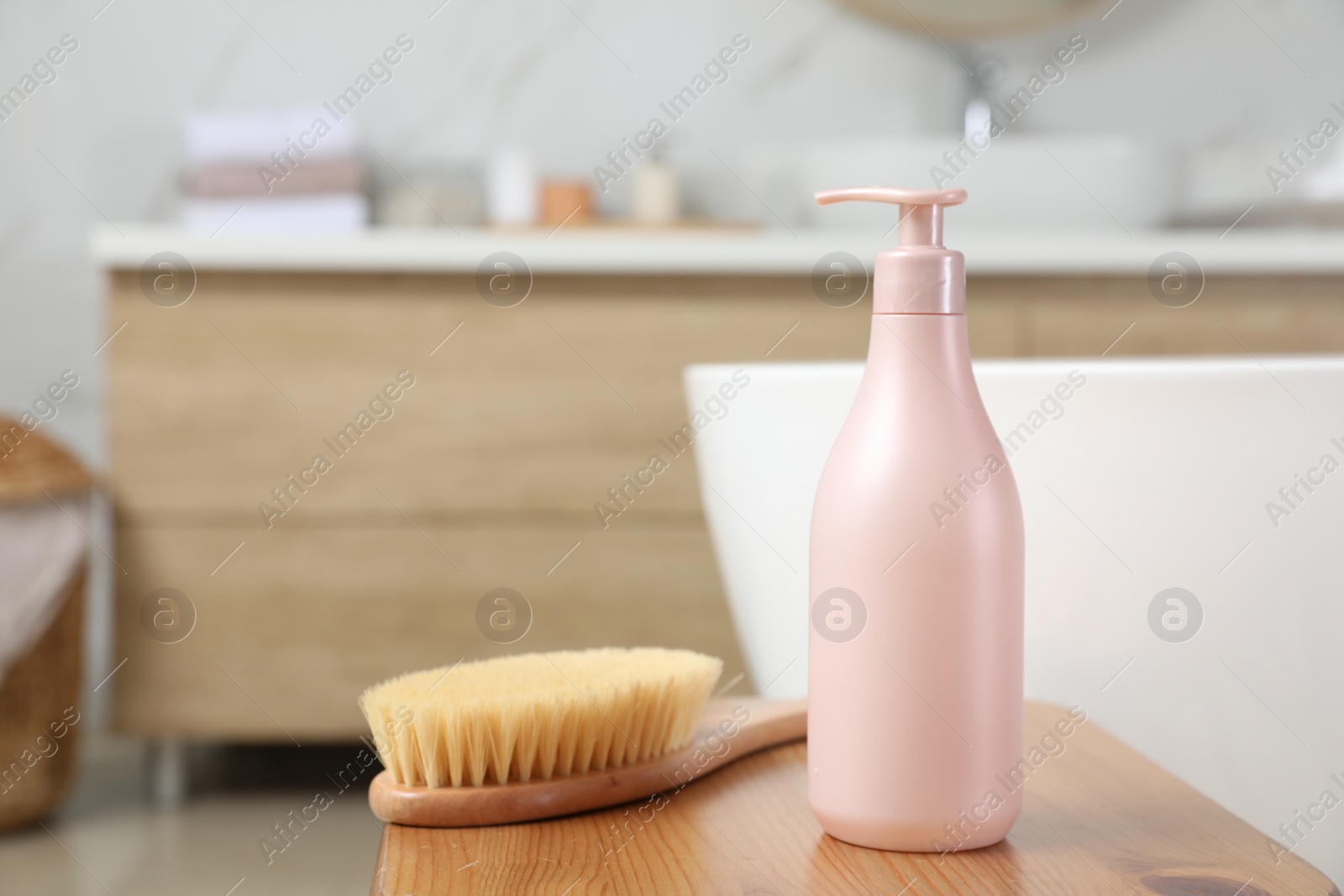 Photo of Bottle of shower gel and brush on wooden table near tub in bathroom, space for text