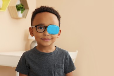 Photo of African American boy with eye patch on glasses in room, space for text. Strabismus treatment