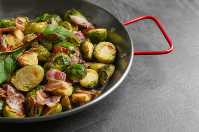 Photo of Delicious roasted Brussels sprouts with bacon in pan on black table, closeup