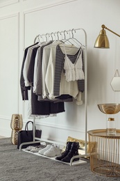 Photo of Rack with stylish clothes near white wall in dressing room
