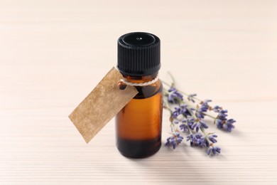 Bottle of essential oil and lavender flowers on white wooden table, closeup