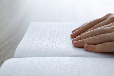 Blind man reading book written in Braille at table, closeup