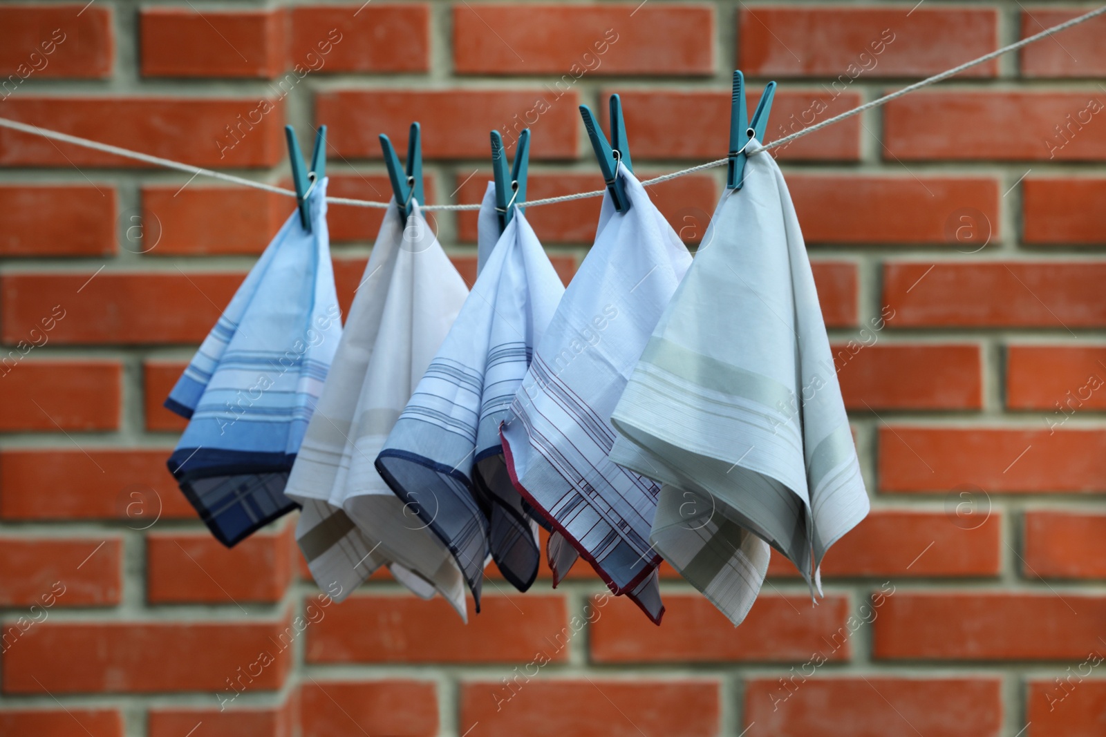 Photo of Different handkerchiefs hanging on rope near red brick wall outdoors