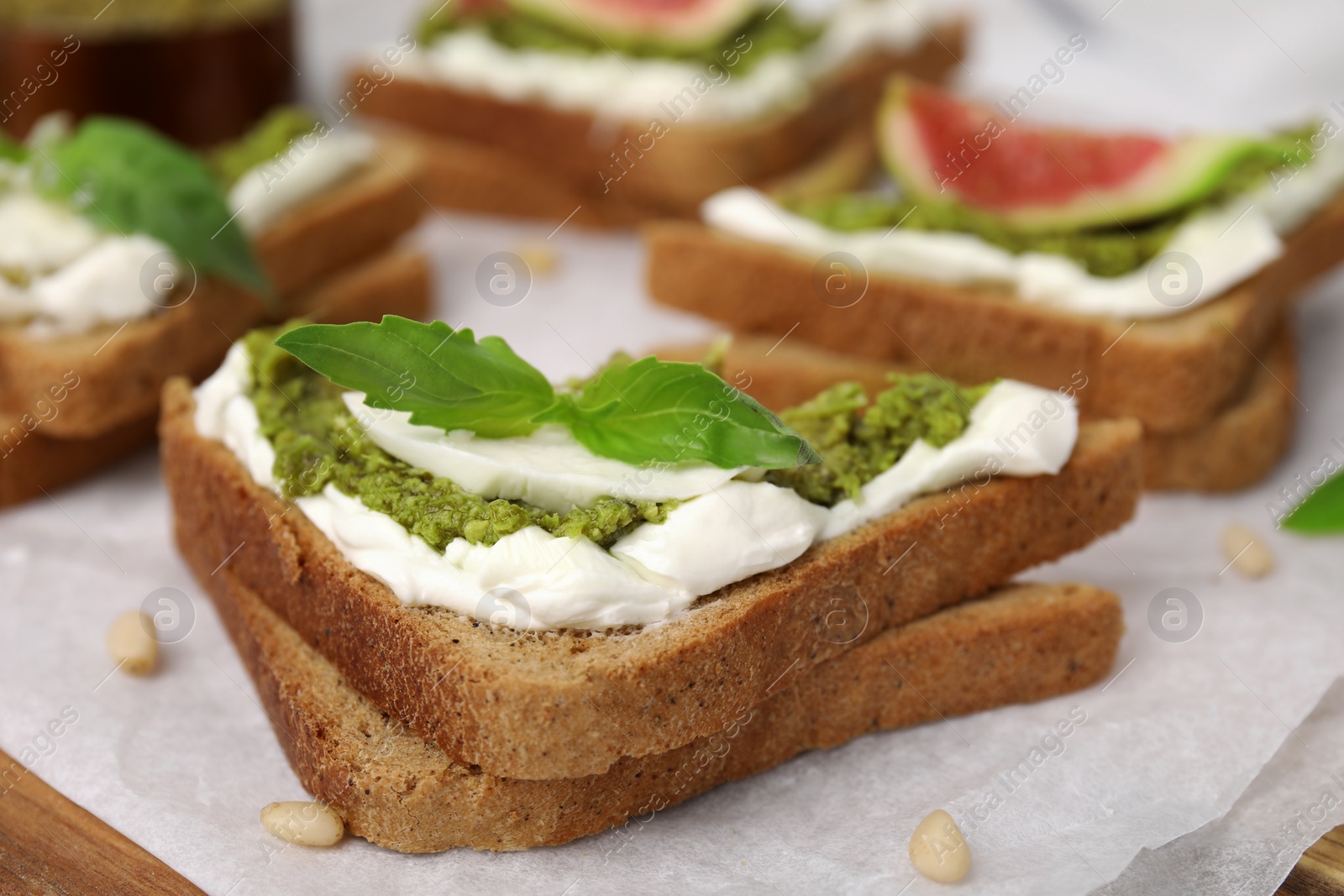 Photo of Tasty bruschetta with cream cheese, pesto sauce and fresh basil on parchment paper, closeup