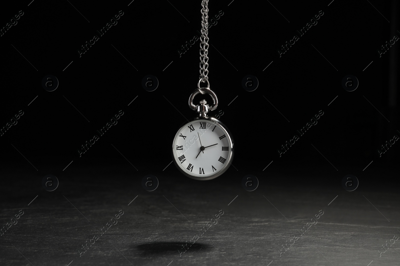 Photo of Beautiful vintage pocket watch with silver chain on black background above dark table. Hypnosis session