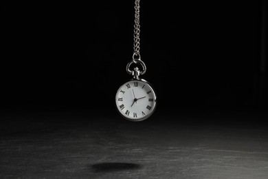Photo of Beautiful vintage pocket watch with silver chain on black background above dark table. Hypnosis session