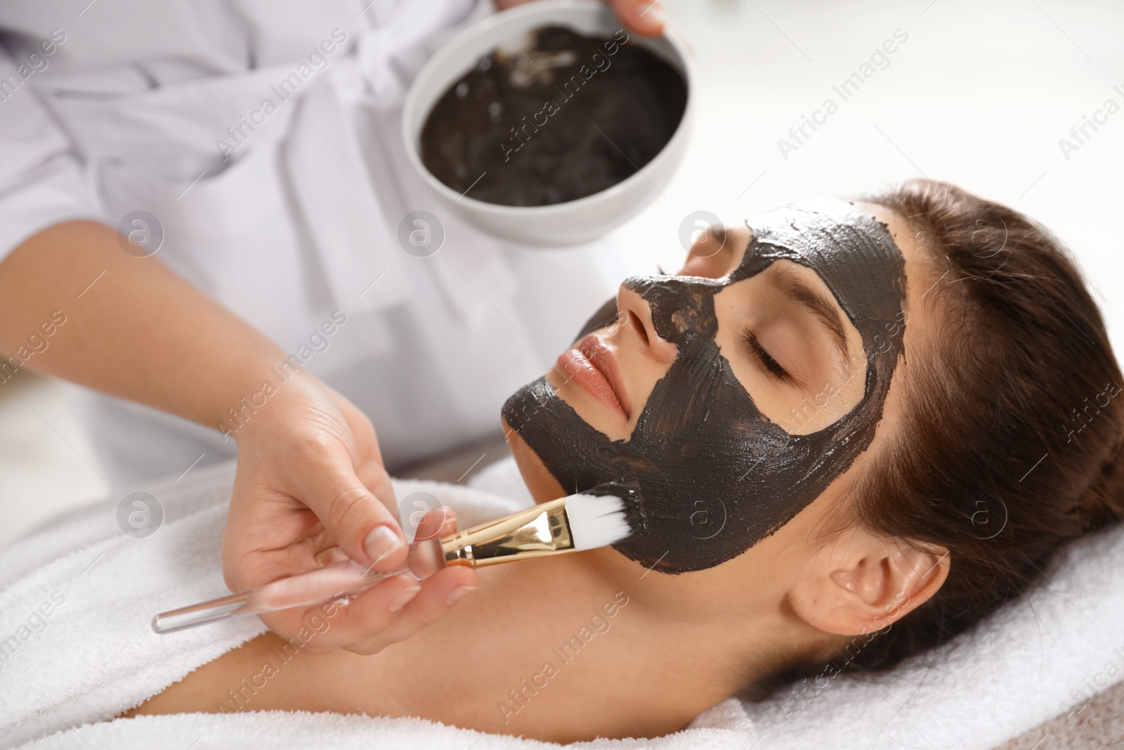 Photo of Cosmetologist applying black mask onto woman's face in spa salon