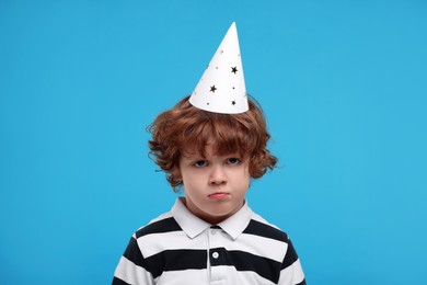 Photo of Sad little boy in party hat on light blue background