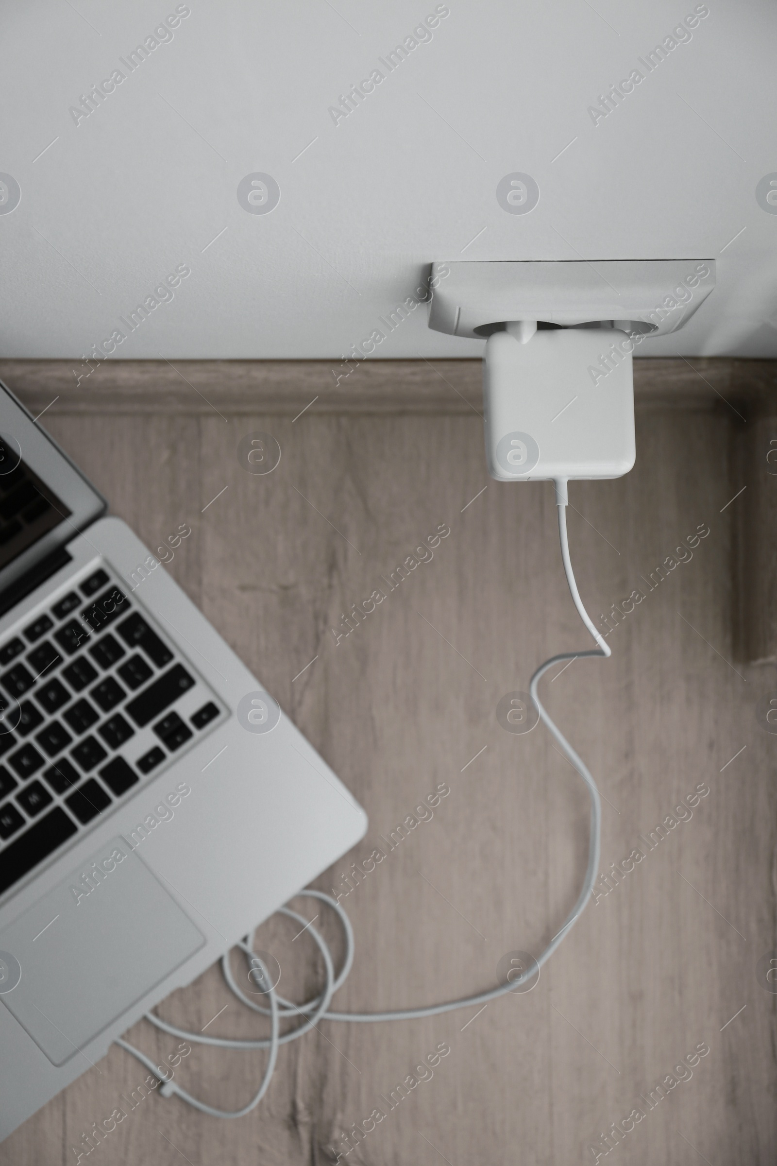 Photo of Modern laptop charging from electric socket, top view