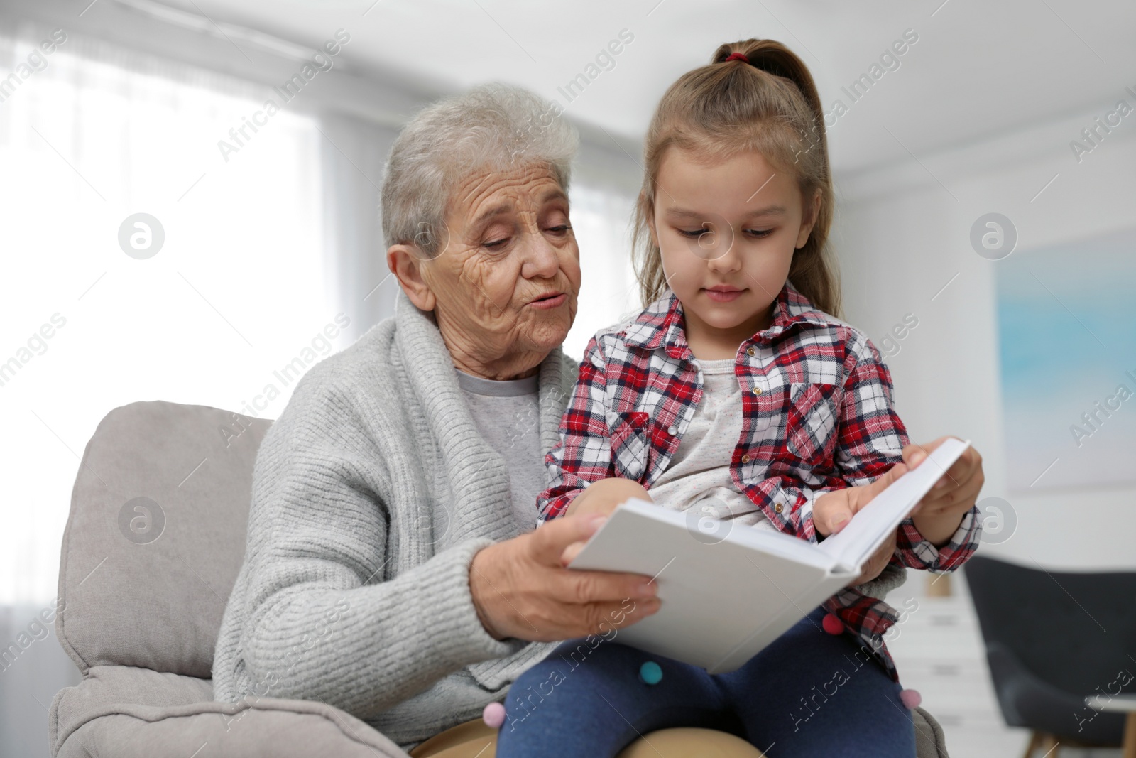 Photo of Cute girl and her grandmother reading book at home