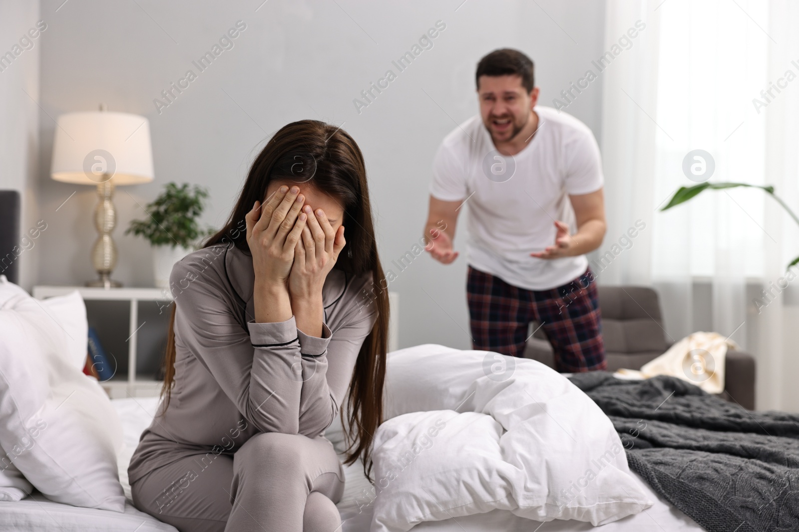 Photo of Wife covering face with hands while her husband screaming in bedroom, selective focus. Relationship problems