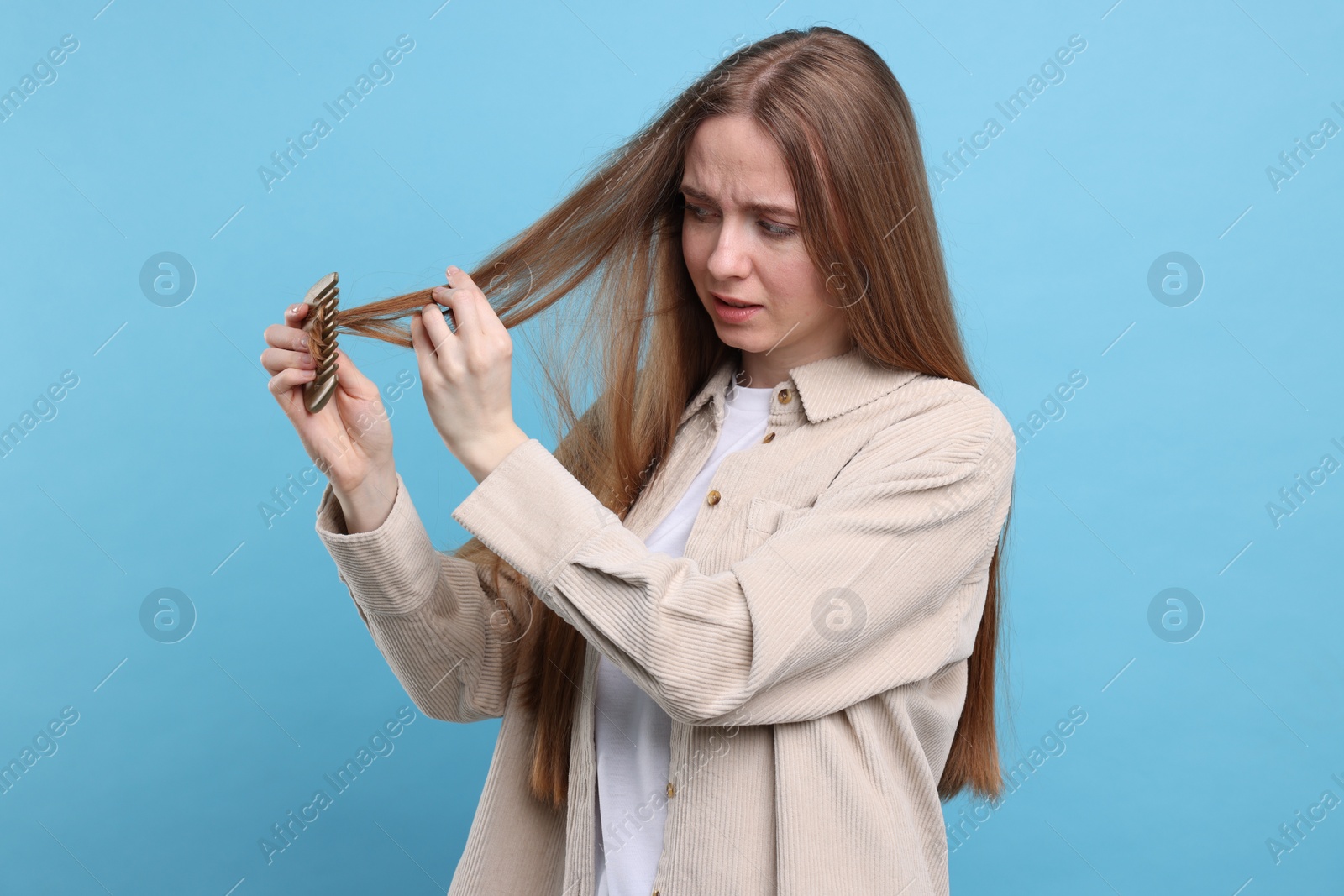 Photo of Emotional woman brushing her hair on light blue background. Alopecia problem