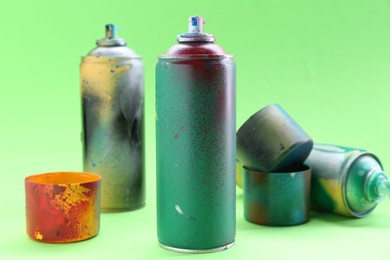 Photo of Spray paint cans with caps on green background, closeup