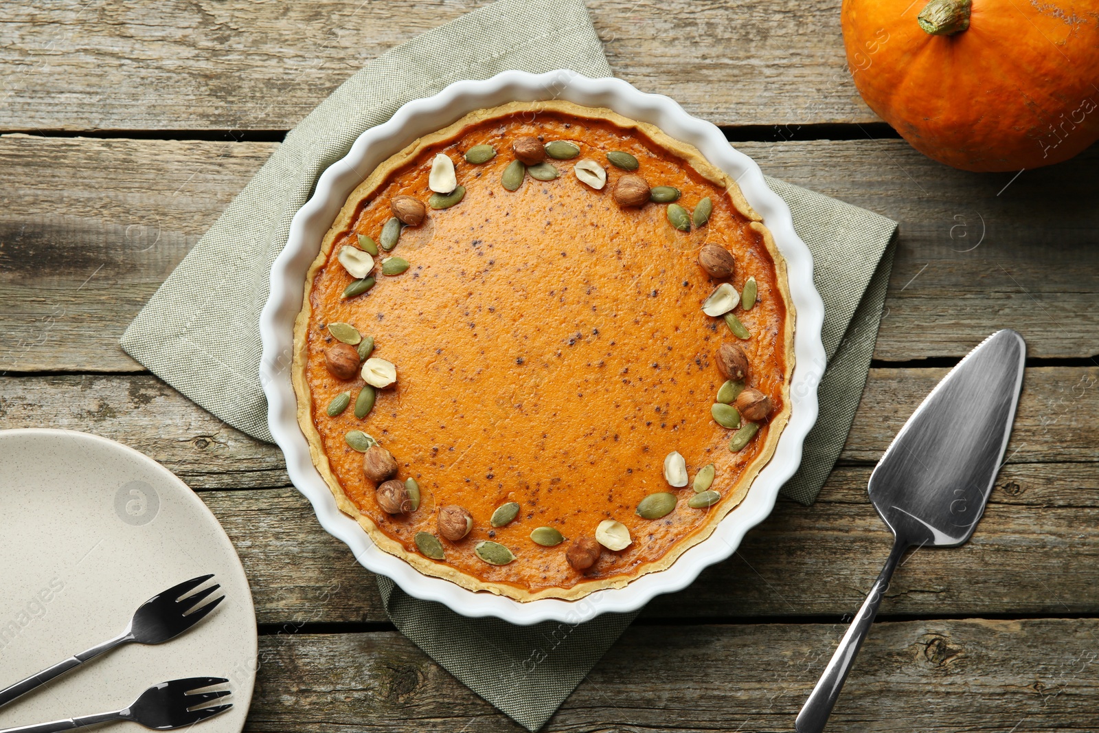 Photo of Delicious pumpkin pie with seeds and hazelnuts served on wooden table, flat lay