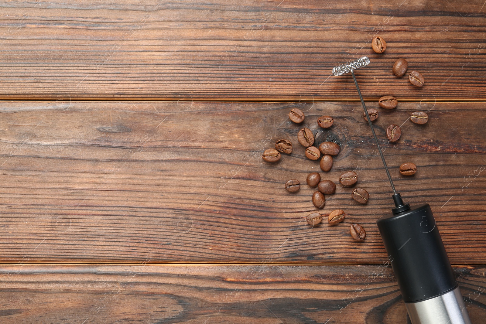 Photo of Black milk frother wand and coffee beans on wooden table, top view. Space for text