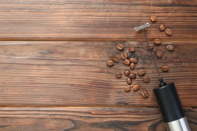 Black milk frother wand and coffee beans on wooden table, top view. Space for text