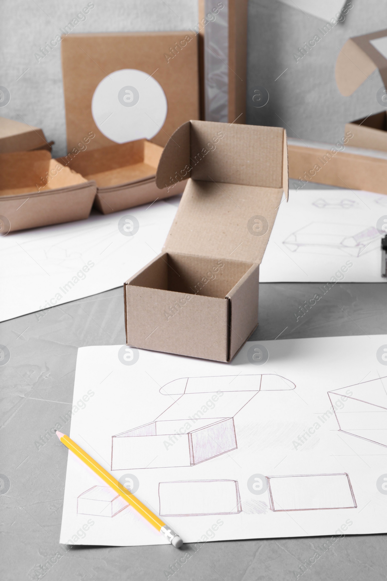 Photo of Creating packaging design. Drawings, boxes and pencil on blue textured table, closeup