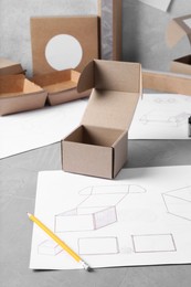 Creating packaging design. Drawings, boxes and pencil on blue textured table, closeup