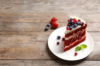 Photo of Plate with piece of delicious homemade red velvet cake and space for text on wooden table