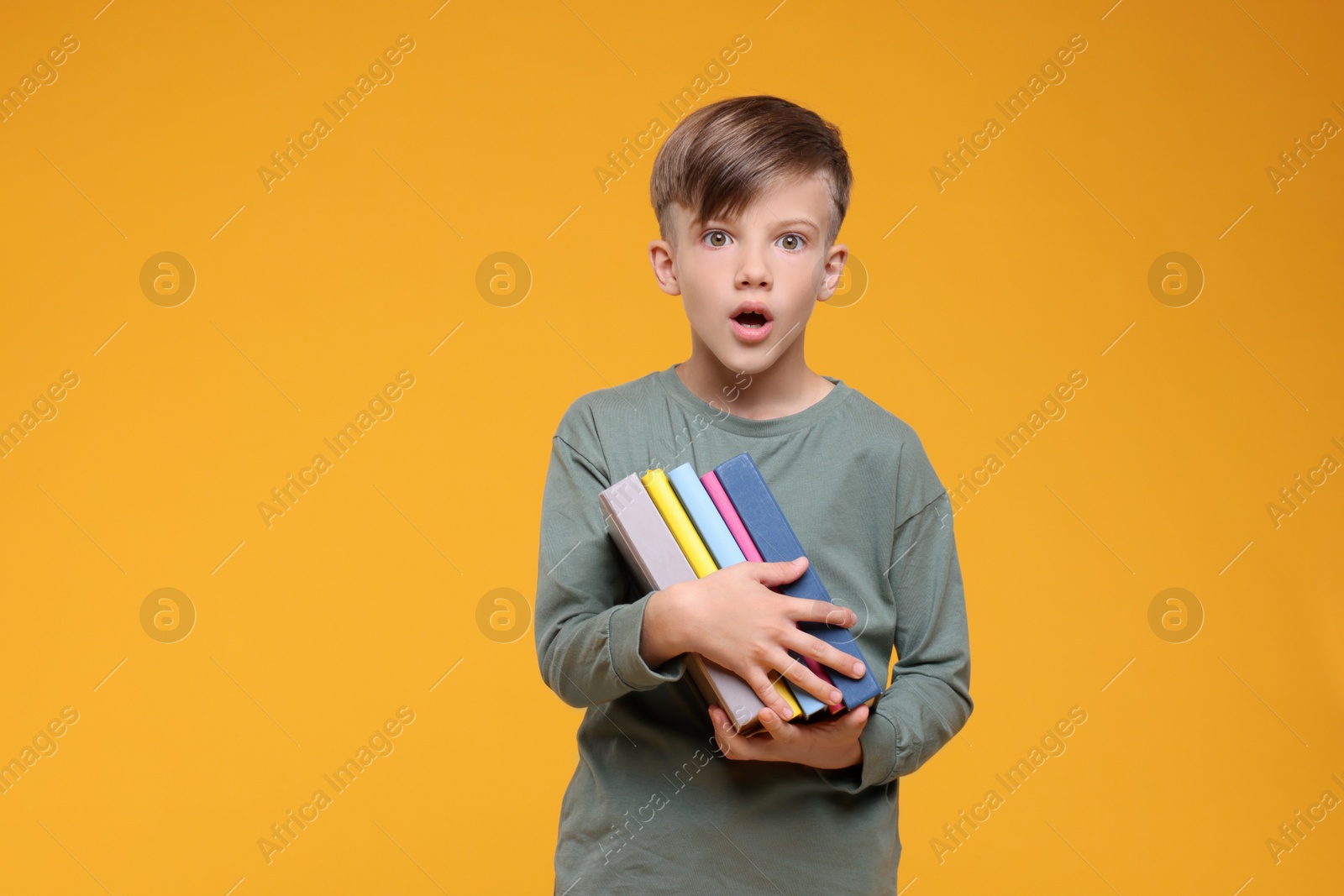 Photo of Surprised schoolboy with books on orange background