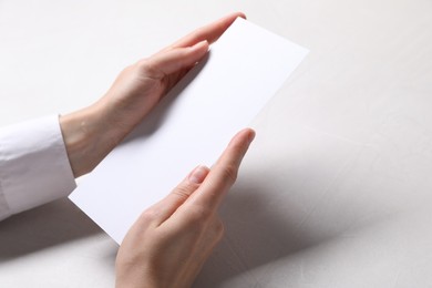 Woman holding blank card at white table, closeup. Mockup for design