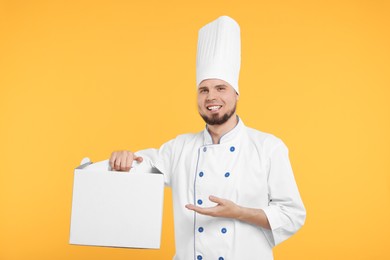 Photo of Happy professional confectioner in uniform holding cake box on yellow background